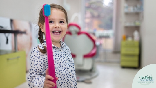 Toddler aged girl holding a large pink toothbrush