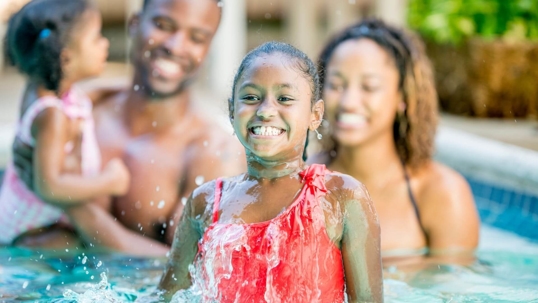 black family with two daughters in a swimming pool and laughing